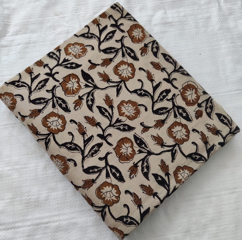May include: A beige cotton fabric with a brown and black floral print. The fabric is folded in half and has a smooth texture.