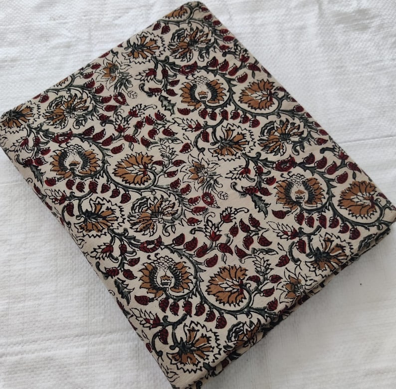 K&ouml;nnte beinhalten: Ein cremefarbener Baumwollstoff mit einem Blumendruck. Die Blumen sind in Braun-, Rot- und Gr&uuml;nt&ouml;nen gehalten. Der Stoff ist in der H&auml;lfte gefaltet und hat eine glatte Textur.