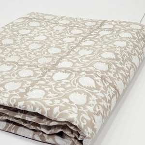 May include: A beige cotton fabric with a white floral print. The fabric is folded in thirds and the pattern is visible on all sides.