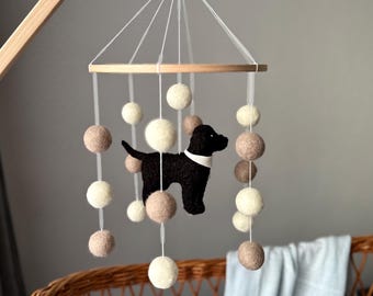 May include: A wooden baby mobile with a black felt dog and white and beige felt balls hanging from it.