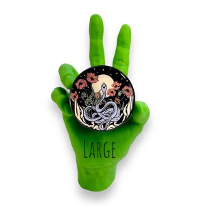 Puede incluir: Un gr&aacute;fico redondo negro y dorado con un dise&ntilde;o de serpiente, flores y luna. La palabra "LARGE" est&aacute; impresa en negro debajo del gr&aacute;fico. El gr&aacute;fico est&aacute; sostenido por una mano verde.