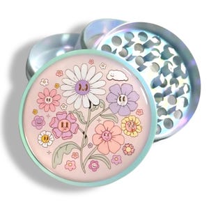 May include: A two-piece, iridescent grinder with a floral design. The top piece is a lid with a series of holes. The bottom piece has a light pink background with a variety of cartoon flowers in shades of pink, purple, yellow, and white.