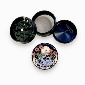 Puede incluir: Molinillo de hierbas negro de cuatro piezas con tapa decorativa. La tapa presenta un dise&ntilde;o de una serpiente morada, flores y una luna. El molinillo incluye una malla y un cepillo peque&ntilde;o. Para hierbas.