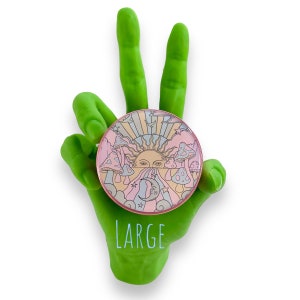 Peut inclure: &Eacute;pinglette ronde &agrave; bord rose, orn&eacute;e d'un soleil, de champignons, d'une lune et d'&eacute;toiles aux couleurs pastel. Le mot "LARGE" est imprim&eacute; en vert. L'&eacute;pinglette est tenue par une main verte en signe de paix.