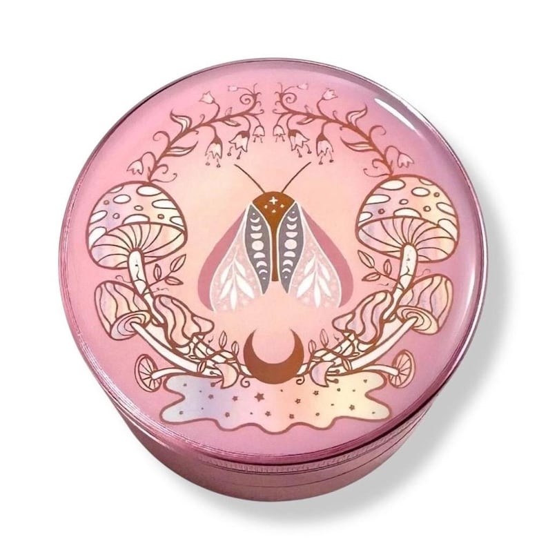 May include: A pink round trinket box with a design of a moth, mushrooms, and a crescent moon. The design is in shades of pink, brown, and white.