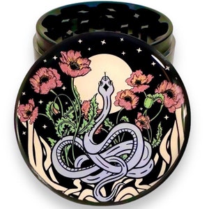 Puede incluir: Un molinillo de hierbas redondo de metal iridiscente con una tapa decorativa. La tapa presenta un dise&ntilde;o de una serpiente morada clara, amapolas rosas, una luna llena y estrellas sobre un fondo negro. El molinillo est&aacute; dise&ntilde;ado para hierbas.