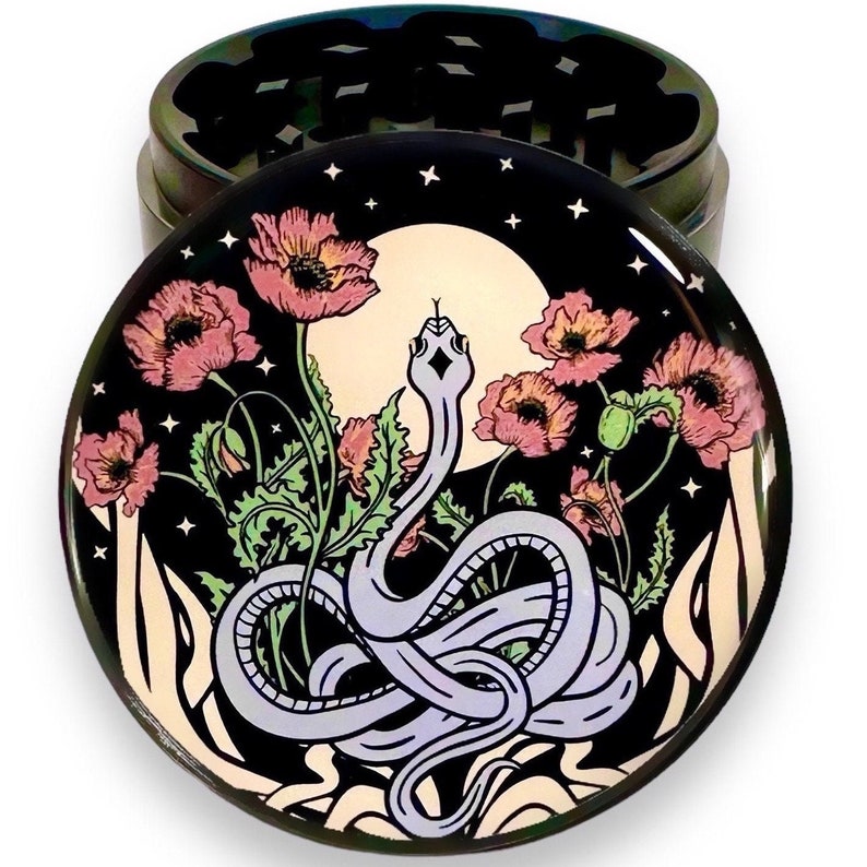 Puede incluir: Un molinillo de hierbas redondo de metal iridiscente con una tapa decorativa. La tapa presenta un dise&ntilde;o de una serpiente morada clara, amapolas rosas, una luna llena y estrellas sobre un fondo negro. El molinillo est&aacute; dise&ntilde;ado para hierbas.