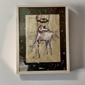 Può includere: Opera d'arte astratta in una cornice di legno chiaro. L'opera presenta un disegno di una creatura su una sedia, con testo da uno sfondo di carta vintage. L'opera d'arte ha un bordo marmorizzato in bianco e nero.