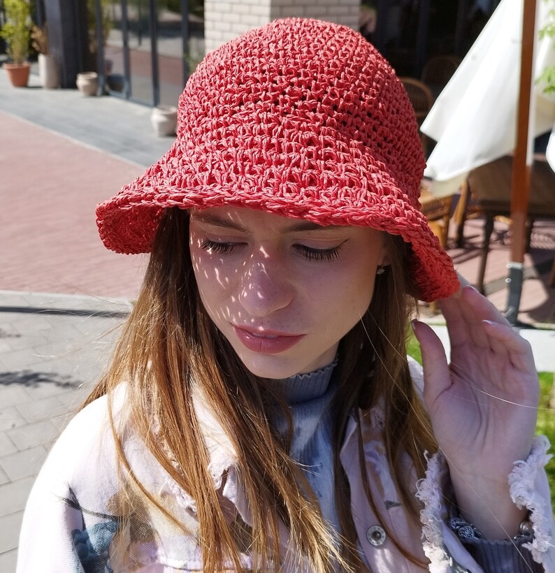 Puede incluir: Una mujer con un sombrero de cubo de crochet rojo y una chaqueta de estampado floral rosa claro y blanco.