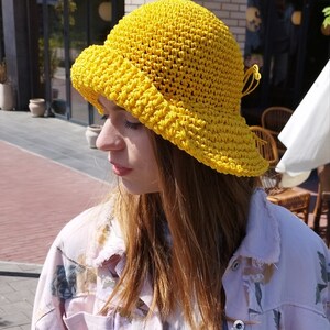Puede incluir: Un sombrero de sol de crochet amarillo con un ala ancha y un lazo atado en un lado.