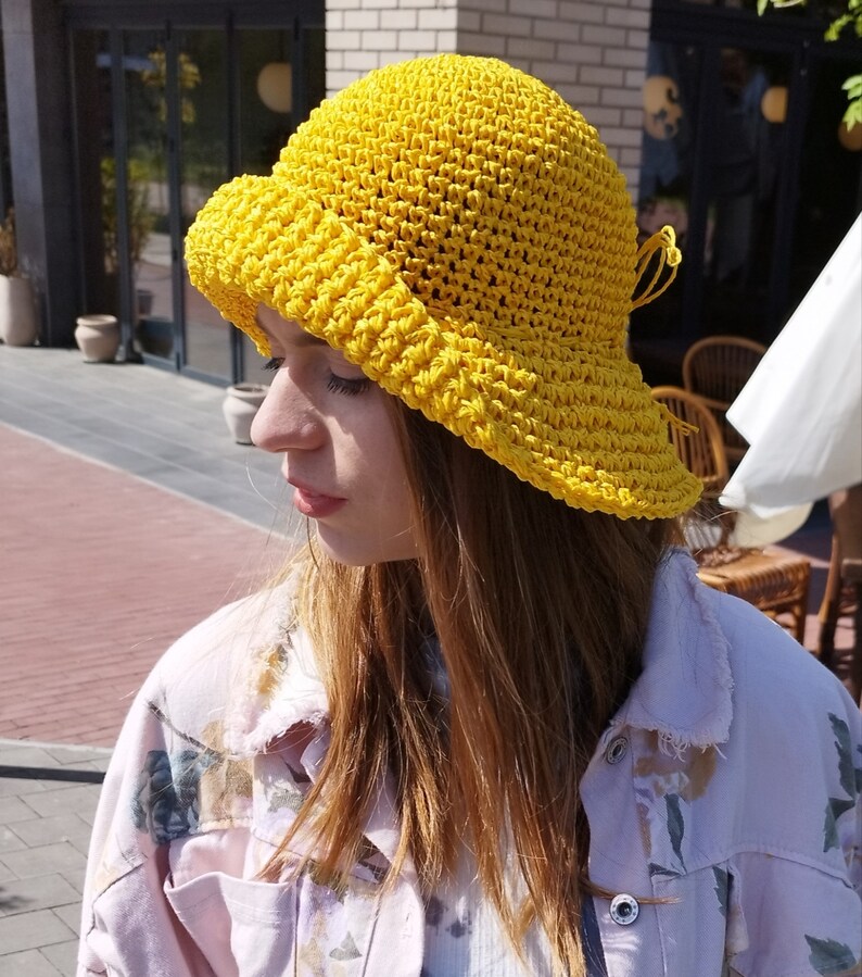 Puede incluir: Un sombrero de sol de crochet amarillo con un ala ancha y un lazo atado en un lado.