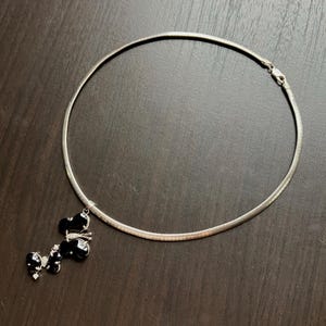 May include: A silver-toned necklace with a black butterfly pendant. The pendant features three black butterfly shapes with small, clear accents. The necklace has a simple, rounded design and a clasp closure.