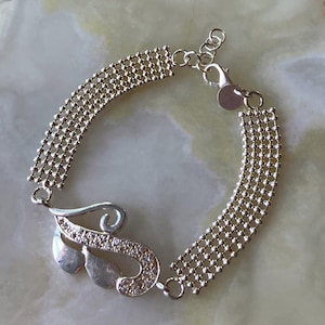 May include: A silver-toned bracelet featuring two sections of fine ball-chain mesh connected by a central decorative element. The centerpiece is a curved, leaf-like shape with a smooth polished finish and a textured section embedded with small clear stones.
