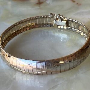 May include: A gold-toned bracelet with a textured, ribbed design. The bracelet features a secure clasp and a flexible, segmented construction. The jewelry piece is likely made of metal and is designed to be worn around the wrist.
