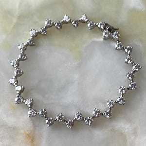 May include: A silver bracelet with a series of clear, round-cut gemstones set in a zig-zag pattern. The bracelet is closed with a small clasp. The gemstones are evenly spaced and reflect light.
