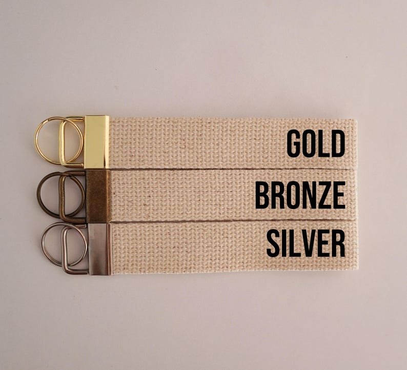 Op de afbeelding: Drie beige canvas sleutelhangers met metalen hardware in goud, brons en zilver. De tekst "GOLD", "BRONZE" en "SILVER" is in zwart op het canvas gedrukt.
