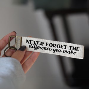 Peut inclure: Porte-clés en toile blanche avec une inscription noire qui dit "N'oubliez jamais la différence que vous faites".