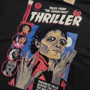 May include: A black t-shirt with a comic book cover design featuring a zombie Michael Jackson from the "Thriller" music video. The cover reads "Tales from 'The Graveyard'" and "Thriller" with a comic book logo.