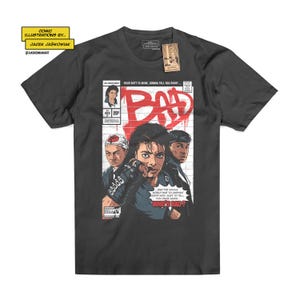 Può includere: Una t-shirt grigio antracite a maniche corte con una stampa grafica in stile fumetto sul davanti. Il design include il testo "BAD" in grandi lettere rosse, illustrazioni di tre persone e il testo "YOUR BUTT IS MINE, GONNA TELL YOU RIGHT" e "WHO'S BAD?"