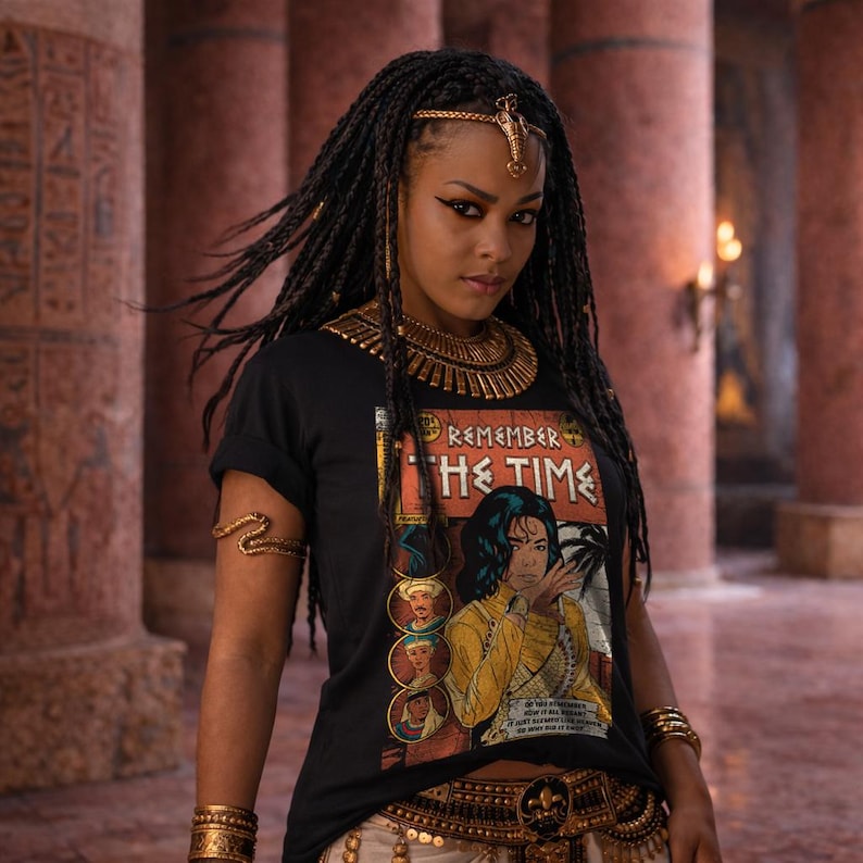 May include: A black t-shirt with the words "REMEMBER THE TIME" and a comic book-style illustration. The shirt is worn with gold jewelry, including a necklace, bracelets, and arm cuffs. The model has long, braided hair and is in a room with columns.