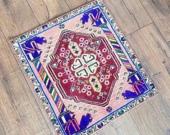 May include: A pink and red patterned rug with a blue, green, and white border. The rug has a traditional design with a central medallion and floral motifs.
