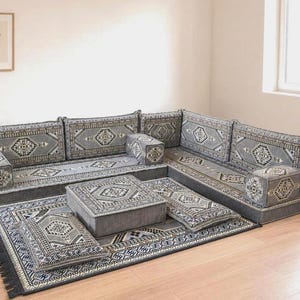 May include: A gray sectional sofa with matching cushions and a rectangular coffee table, all adorned with intricate geometric patterns. The set is placed on a large area rug with a similar design, creating a cohesive living space.