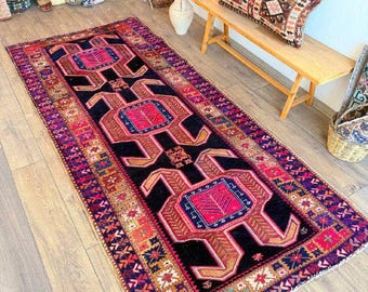 May include: A rectangular area rug featuring a black central field with three large, symmetrical geometric medallions in vibrant pink and blue. The border displays intricate multi-colored patterns in shades of red, orange, and navy blue.