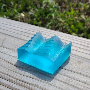 Op de afbeelding: Een doorschijnend blauw plastic object in de vorm van een golf met een getextureerd oppervlak. Het object is gemaakt van helder plastic en heeft een gladde, afgeronde vorm.