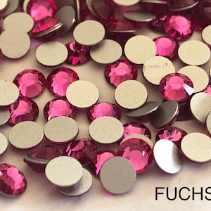 May include: A close-up of a large quantity of fuchsia-colored rhinestones with silver backing. The rhinestones are scattered on a white surface. The word "FUCHSIA" is written in black letters at the bottom of the image.