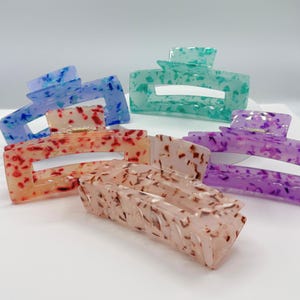 May include: Set of five hair clips in various colors, including red, purple, blue, green, and white. The clips are made of plastic and have a speckled pattern.