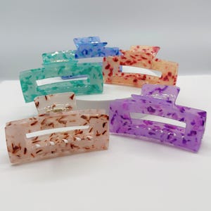 May include: Five colorful hair clips with a speckled pattern. The clips are in shades of blue, green, red, purple, and brown.