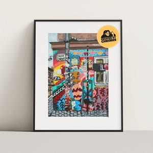 Puede incluir: Una escena callejera colorida con un edificio cubierto de grafitis. El edificio está pintado en una variedad de colores, incluyendo rojo, azul, verde, amarillo y rosa. También hay varios letreros y carteles en el edificio. La calle está pavimentada con adoquines y hay árboles y plantas en el fondo.