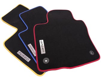 May include: Three black car floor mats with colored fabric edges in yellow, blue, and red. Each mat features a rectangular metal badge with the text TURBO, PREMIUM, or SPORT. The mats include circular mounting holes for secure vehicle installation.