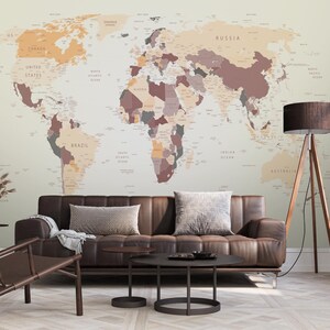 May include: A brown leather sofa with two pillows sits in front of a wall with a world map wallpaper. The map is in shades of beige, brown, and red. A brown floor lamp with a wooden tripod stand is in the corner of the room.