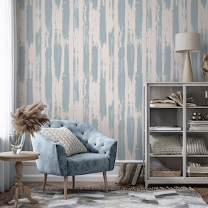 Könnte beinhalten: Ein Wohnzimmer mit einem blauen Sessel, einem kleinen Beistelltisch aus Holz und einem gemusterten Teppich. Die Wand hat ein vertikales Pinselstrich-Design in Hellblau und Off-White. Ein weißer Schrank und eine Lampe sind ebenfalls zu sehen.