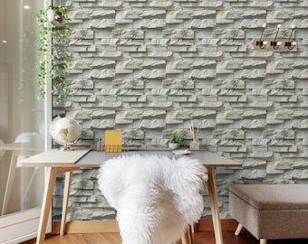 May include: An office space with a light wood desk, a white fluffy chair, and a gray ottoman. The wall is covered in a textured, light gray stone pattern. A globe, small plant, and notepad sit on the desk. The floor is wood.