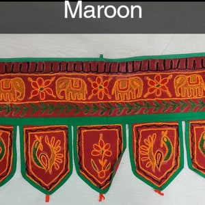 May include: Maroon fabric door hanging with a green border and embroidered elephants, flowers, and peacocks. The hanging has a scalloped bottom with tassels.