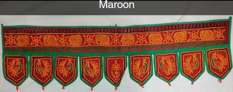 May include: Maroon fabric door hanging with a green border and embroidered elephants, flowers, and peacocks. The hanging has a scalloped bottom with tassels.