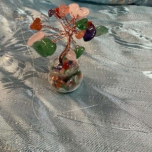 May include: A small wire tree sculpture with heart-shaped gemstones in shades of pink, green, purple, and red. The tree is in a clear glass vase filled with smaller gemstones.