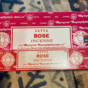 May include: A red and white box of Satya Rose incense sticks. The box features the brand name "Shrinivas Sugandhalaya" and the text "Satya Rose Incense". The box is 15 grams.