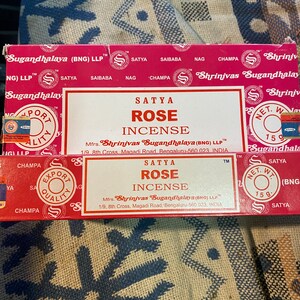 May include: A red box of Satya Rose incense sticks. The box has a white border and features the text "Satya Rose Incense" and the company name "Shrinivas Sugandhalaya (BNG) LLP".