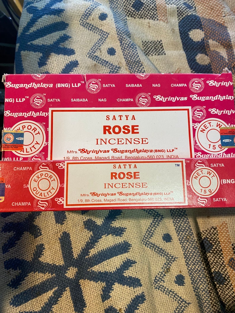 May include: A red box of Satya Rose incense sticks. The box has a white border and features the text "Satya Rose Incense" and the company name "Shrinivas Sugandhalaya (BNG) LLP".