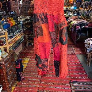May include: Red, black, and orange patchwork pants with a drawstring waist and floral print. The pants are made of a soft, lightweight fabric and have a relaxed fit.