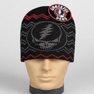 May include: Black knit beanie featuring a Steal Your Face skull design in gray. The hat has red and gray zigzag patterns and a circular tag with the words "Grateful Dead" and a logo. The beanie is displayed on a mannequin head.