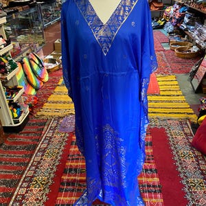 May include: A long, flowing blue kaftan with gold embroidery. The kaftan has a V-neck and a drawstring waist. It is made of a soft, lightweight fabric.