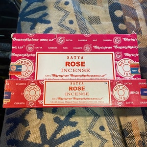 May include: A red and white box of Satya Rose incense sticks. The box features the brand name "Shrinivas Sugandhalaya" and the text "Net. Wt. 15g".