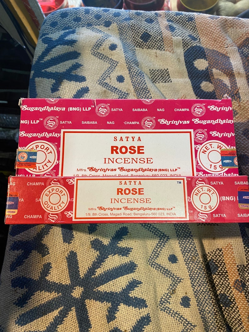 May include: A red and white box of Satya Rose incense sticks. The box features the brand name "Shrinivas Sugandhalaya" and the text "Net. Wt. 15g".