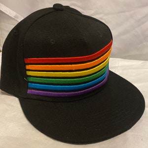 May include: A black baseball cap with a rainbow stripe design. The cap has a curved brim and a flat top.