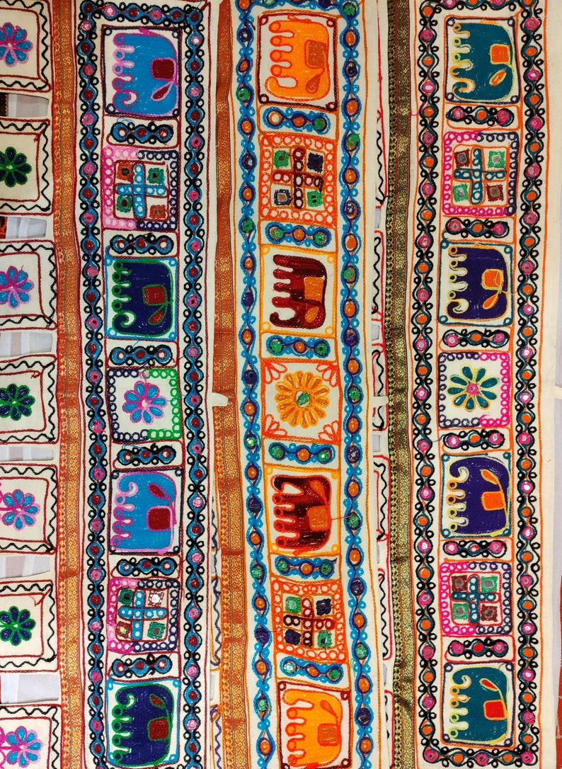 May include: Three strips of white fabric with colorful embroidered designs. Each strip features repeating patterns of elephants, flowers, and geometric shapes. The fabric is trimmed with gold and silver thread.