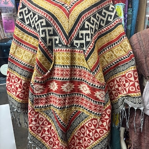 May include: A white ceramic mug with a black handle and the text "But First, Coffee" in a bold, black font. The mug is set against a blurred background, suggesting a cozy setting.